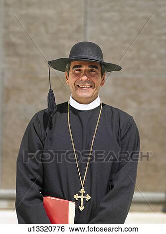 Stock Photograph - Head and shoulders portrait of priest by ornate door, Alicante, Spain,. Fotosearch