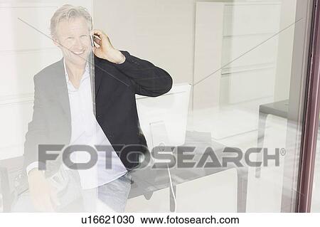 Stock Image - Man in office on telephone with reflections.. Fotosearch