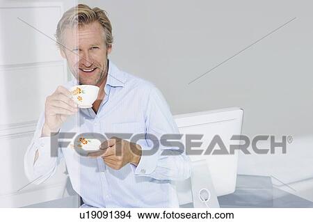 Picture - Man in office with cup of tea smiling with reflections.. Fotosearch