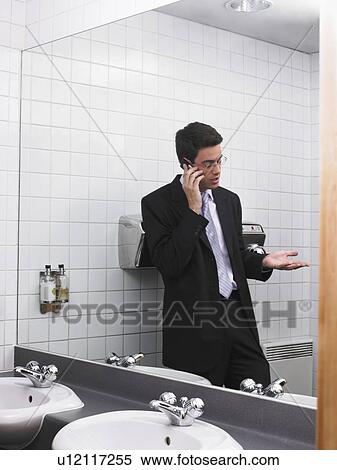 Man reflected in office washroom mirror using mobile phone View Large Photo Image Stock Photography - Man reflected in office washroom mirror using mobile phone. Fotosearch
