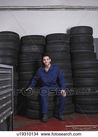 Picture - Mechanic sitting on a stack of tires. Fotosearch