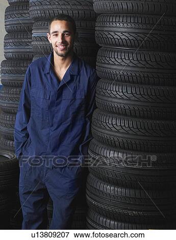 Stock Photo - Mechanic standing by stacks of tires. Fotosearch