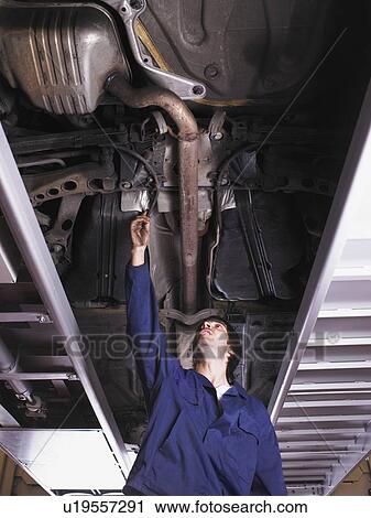 Stock Image - Mechanic standing under raised car. Fotosearch