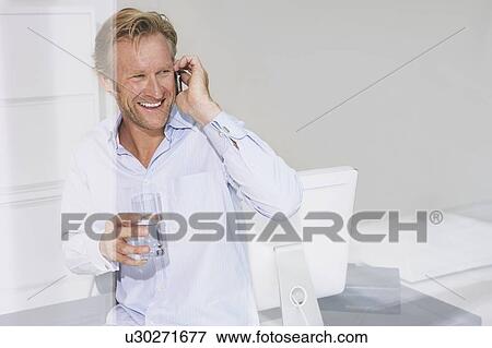 Stock Photo - Smiling man in office on phone.. Fotosearch