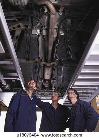 Three mechanics standing under a raised car View Large Photo Image Picture - Three mechanics standing under a raised car. Fotosearch