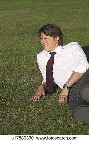Stock Image - Businessman sitting in meadow laughing.. Fotosearch