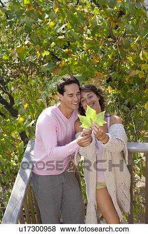 Stock Photo - Couple standing on balcony holding leaf smiling.. Fotosearch