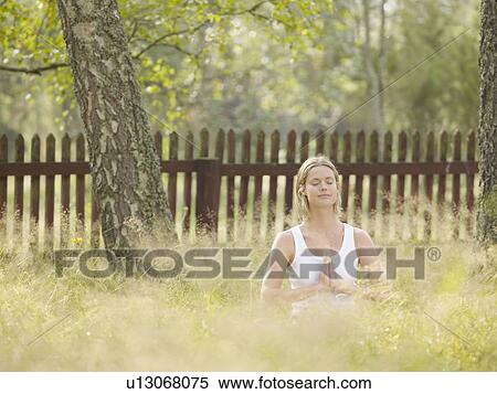 Woman sitting in the grass by a wooden fence doing yoga. View Large Photo Image Stock Photography - Woman sitting in the grass by a wooden fence doing yoga.. Fotosearch