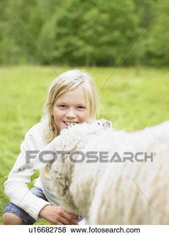 Young girl smiling and crouching by a sheep in a field. View Large Photo Image Stock Photo - Young girl smiling and crouching by a sheep in a field.. Fotosearch