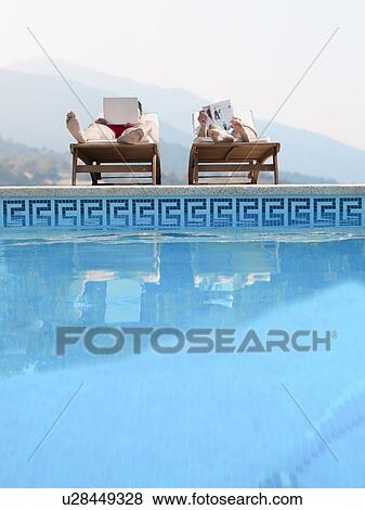 Couple sunbathing by swimming pool, man using laptop View Large Photo Image Stock Photo - Couple sunbathing by swimming pool, man using laptop. Fotosearch