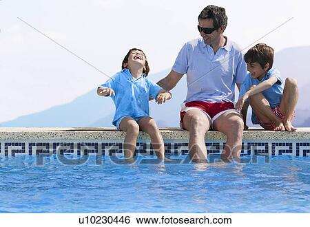 Stock Photograph - Father sitting by swimming pool with two sons (5-7). Fotosearch