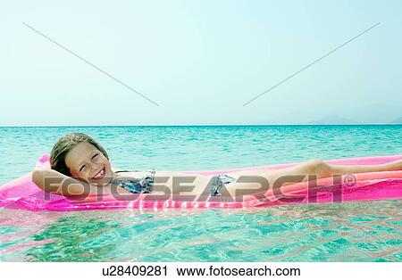 Stock Image - Young girl lying on inflatable raft in the water smiling.. Fotosearch
