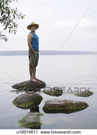 Man standing on stone in water View Large Photo Image Stock Image - Man standing on stone in water. Fotosearch