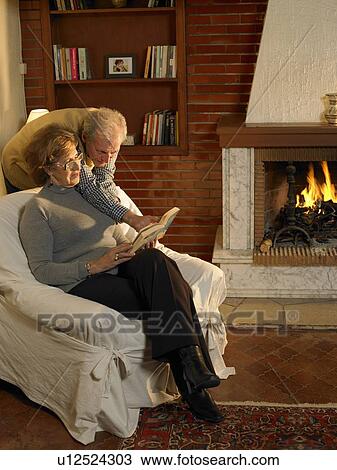 Stock Image - Senior couple looking at book in living room. Fotosearch