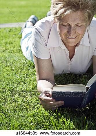 Stock Photography - Woman lying on grass reading. Fotosearch