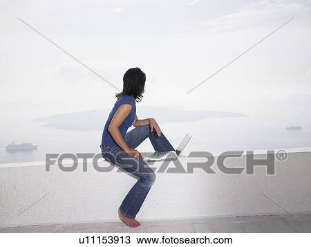 Woman with laptop sitting on a low wall View Large Photo Image Stock Image - Woman with laptop sitting on a low wall. Fotosearch