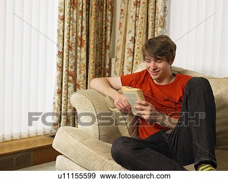 Young man relaxing on sofa reading book View Large Photo Image Stock Photo - Young man relaxing on sofa reading book. Fotosearch