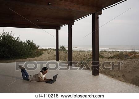 Young woman using laptop on beach patio View Large Photo Image Stock Photograph - Young woman using laptop on beach patio. Fotosearch