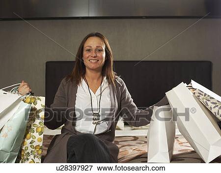 Stock Photo - Mature woman on bed with shopping bags. Fotosearch
