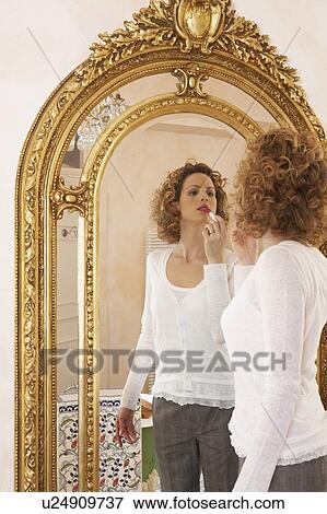 Stock Photo - woman applying lipstick in mirror. Fotosearch
