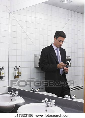 Man reflected in office washroom mirror using mobile phone View Large Photo Image Stock Photograph - Man reflected in office washroom mirror using mobile phone. Fotosearch