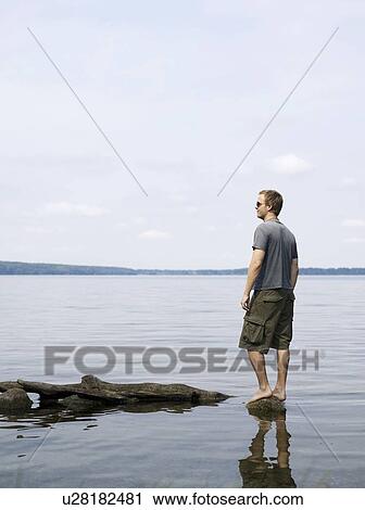 Man standing on rock in shallow water View Large Photo Image Stock Image - Man standing on rock in shallow water. Fotosearch