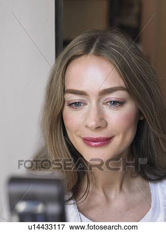 Stock Photo - Woman looking at mobile phone, smiling, close-up. Fotosearch