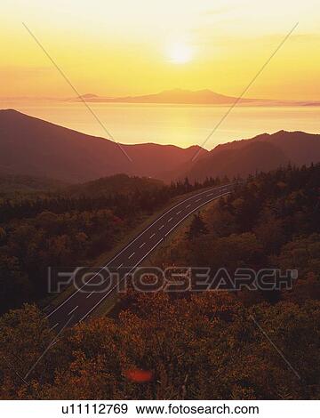 Stock Photo -  a Country Road, Surrounded By Trees and Mountains By Sunset, High Angle View. Fotosearch