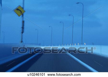 Stock Image -  a Highway With Several Streetlamps and a Road Sign on the Side, Front View, Blurred Motion, Toned Image. Fotosearch