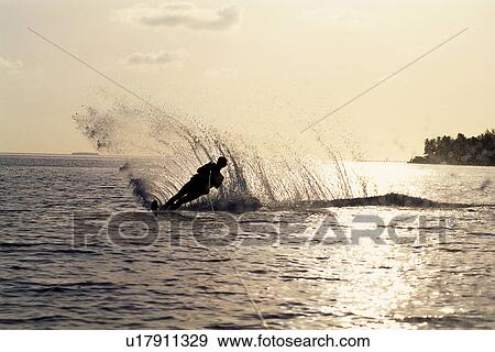 Stock Photo -  a Person Doing Water Ski, the Water Splashing in Many Directions, Maldives, Micronesia, Toned Image. Fotosearch