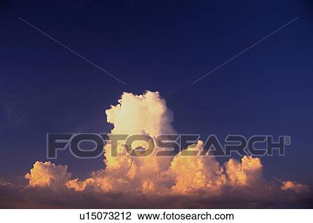 Stock Image -  Several Clouds Under a Deep Blue Sky, Orange-colored From the Setting Sun, Low Angle View. Fotosearch