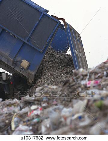 Stock Image - Bulldozer spreading trash in landfill, low angle view, Differential Focus. Fotosearch