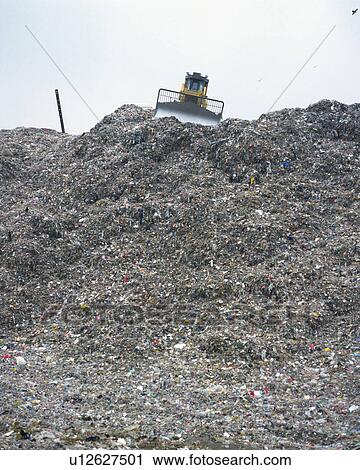 Stock Image - Bulldozer spreading trash in landfill, low angle view . Fotosearch