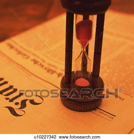 Stock Image - A sand clock on the newspaper, Close Up, High Angle View, Toned Image. Fotosearch