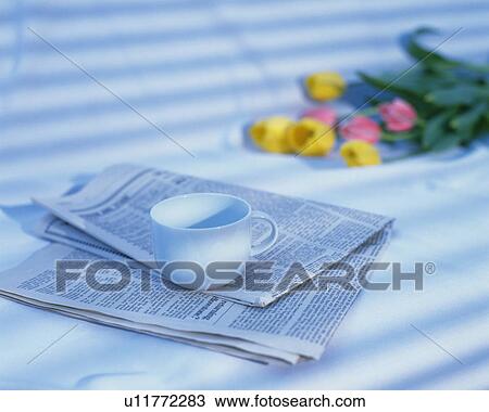 Stock Image - Cup on newspaper and floers, Close Up, High Angle View, Differential Focus, Toned Image. Fotosearch