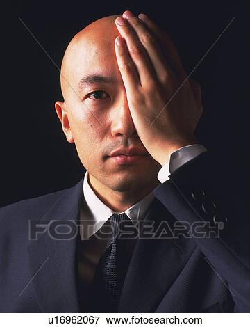 Stock Photo - A bald headed businessman covering an eye with hand, Front View. Fotosearch