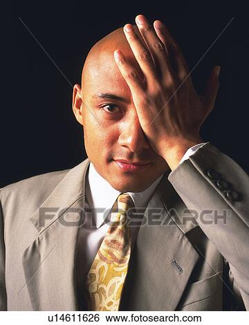 Stock Photograph - A bald headed businessman covering an eye with hand, Front View. Fotosearch