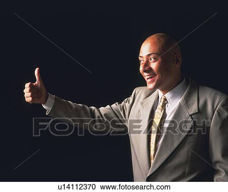Stock Image - A bald headed businessman holding thumb up, Side View. Fotosearch