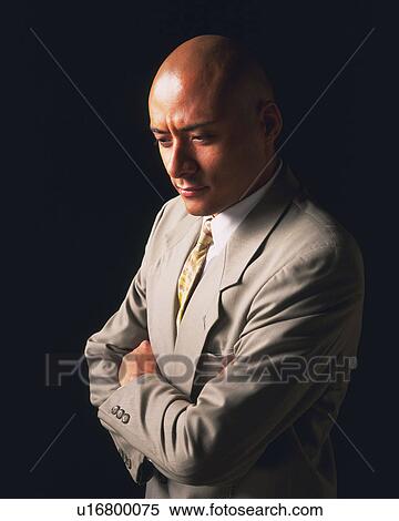 Stock Photography - A bald headed businessman thinking with arms crossed, High Angle View. Fotosearch