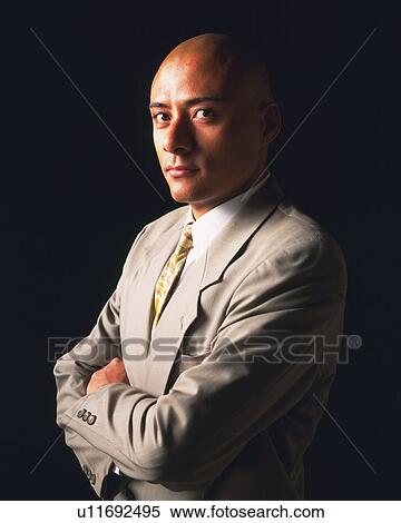Stock Photography - A bald headed businessman with arms crossed, Side View. Fotosearch