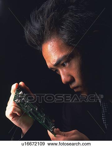 Stock Photo - A businessman holding and looking at the electrical device, Side View. Fotosearch