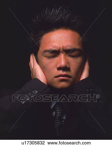 Stock Image - A businessman with eyes closed and covering ears by hands, Front View. Fotosearch