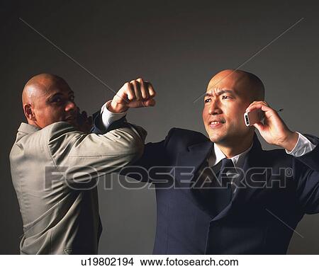 Picture - Two bald headed businessmen crossing arms and talking on mobile phone. Fotosearch