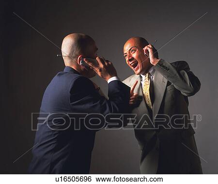Stock Photograph - Two bald headed businessmen laughing and talking on mobile phones, Side View. Fotosearch