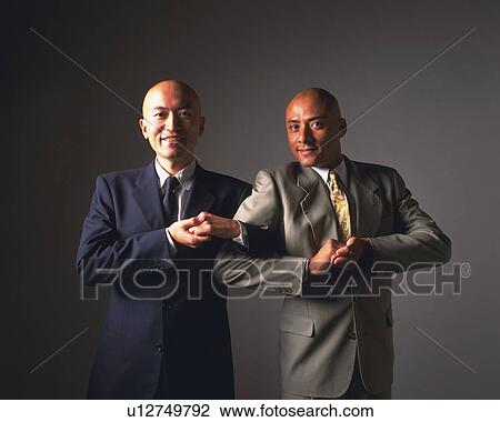 Stock Image - Two bald headed businessmen smiling and crossing arms, Front View. Fotosearch