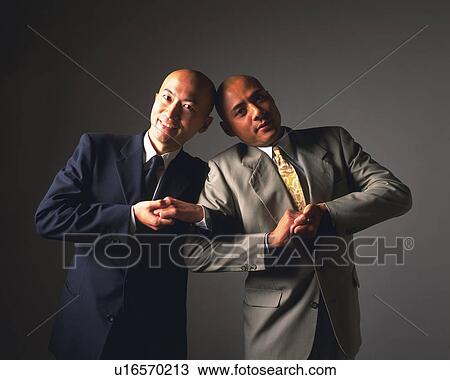 Stock Image - Two bald headed businessmen smiling and posing at camera, Front View . Fotosearch