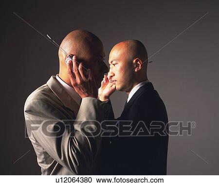 Stock Image - Two bald headed businessmen talking on mobile phones, Side View. Fotosearch