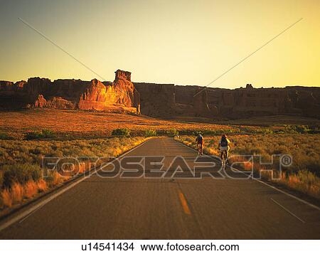 an Asphalt Road With Two Cyclists By Sunset, Surrounded By a Huge Flat Land, High Angle View View Large Photo Image Picture - an Asphalt Road With Two Cyclists By Sunset, Surrounded By a Huge Flat Land, High Angle View . Fotosearch