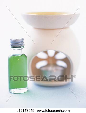 Stock Photo -  a Bottle of Green-colored Aroma Oil Standing Next to an Aroma Pot, Differential Focus. Fotosearch