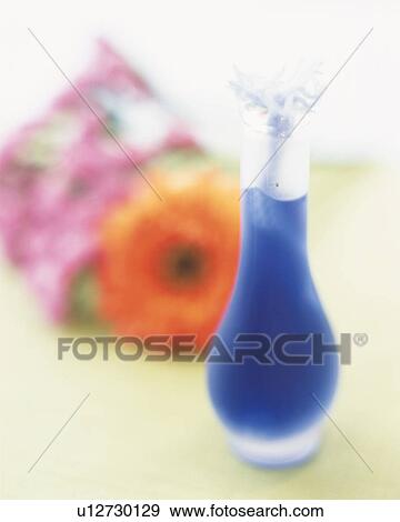 Stock Photo -  a Little Vase With Some Blue Liquid Inside, Next to an Orange Flower, Soft Focus, High Angle View. Fotosearch